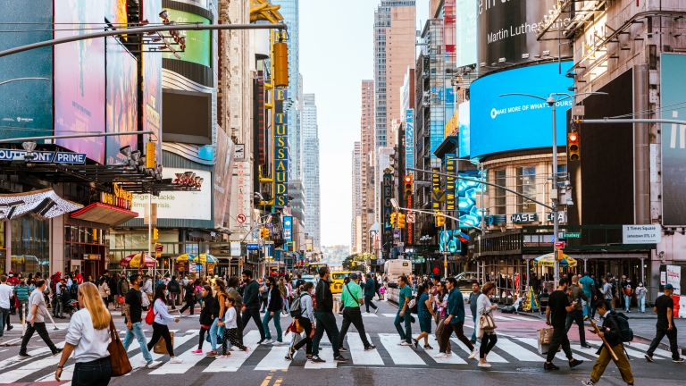 A bustling Times Square street scene in New York City with numerous people crossing at a crosswalk. Neon advertisements and tall buildings line the streets. The sky is clear, and the atmosphere is lively and vibrant. A bustling Times Square street scene in New York City with numerous people crossing at a crosswalk. Neon advertisements and tall buildings line the streets. The sky is clear, and the atmosphere is lively and vibrant.