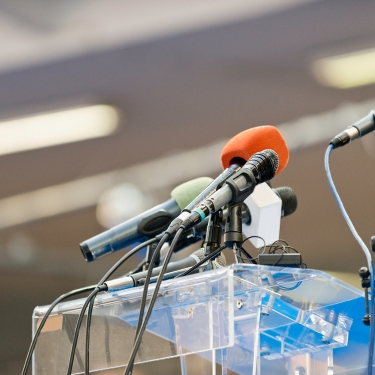 Multiple microphones in various colors are set up on a clear podium, ready for a speech or press conference. The background is blurred, focusing attention on the microphones. Multiple microphones in various colors are set up on a clear podium, ready for a speech or press conference. The background is blurred, focusing attention on the microphones.
