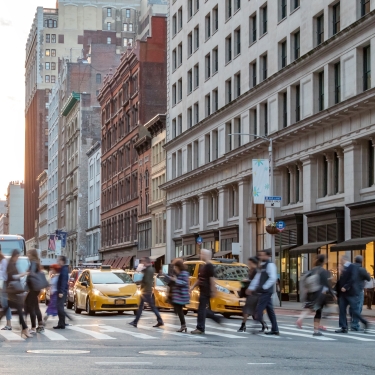 A busy city street scene at sunset with people crossing the street. Yellow taxis and a bus are visible amidst tall buildings, capturing the hustle and bustle of urban life. A busy city street scene at sunset with people crossing the street. Yellow taxis and a bus are visible amidst tall buildings, capturing the hustle and bustle of urban life.