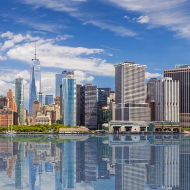 New York City skyline with Financial District and World Trade Center reflected in water of New York Harbor.