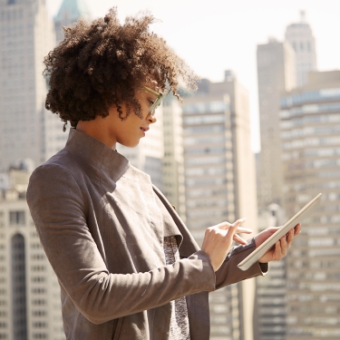 Businesswoman on rooftop holding a tablet computer with the New York City skyline in the background.