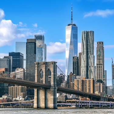 New York City's Brooklyn Bridge spans over the East River against the backdrop of the distinctive Manhattan skyline featuring the One World Trade Center on a sunny day with vibrant blue skies. New York City's Brooklyn Bridge spans over the East River against the backdrop of the distinctive Manhattan skyline featuring the One World Trade Center on a sunny day with vibrant blue skies.
