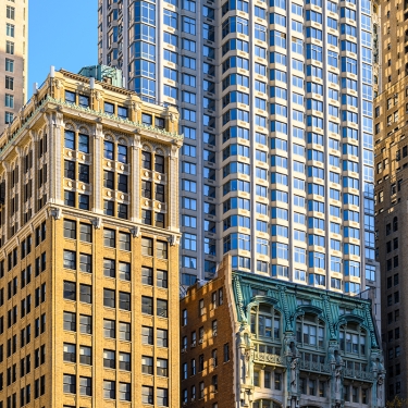 Tall skyscrapers with diverse architectural styles are clustered together under a clear blue sky. Buildings feature brick, stone, and modern facades with numerous windows, reflecting a blend of historic and contemporary design. Tall skyscrapers with diverse architectural styles are clustered together under a clear blue sky. Buildings feature brick, stone, and modern facades with numerous windows, reflecting a blend of historic and contemporary design.