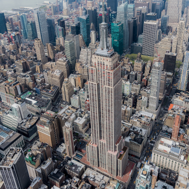 Aerial view of the Empire State Building surrounded by densely packed skyscrapers and New York City streets in Midtown Manhattan on a clear day.